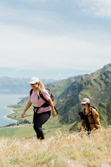 Hikers summit ridge with lake and mountains behind them