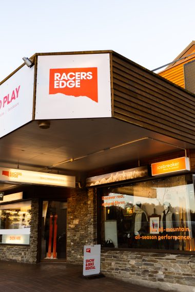 Racers Edge Wānaka storefront, a Love Wanaka Impact Partner, showcasing their outdoor retail location at dusk with illuminated signage on Mount Aspiring Road