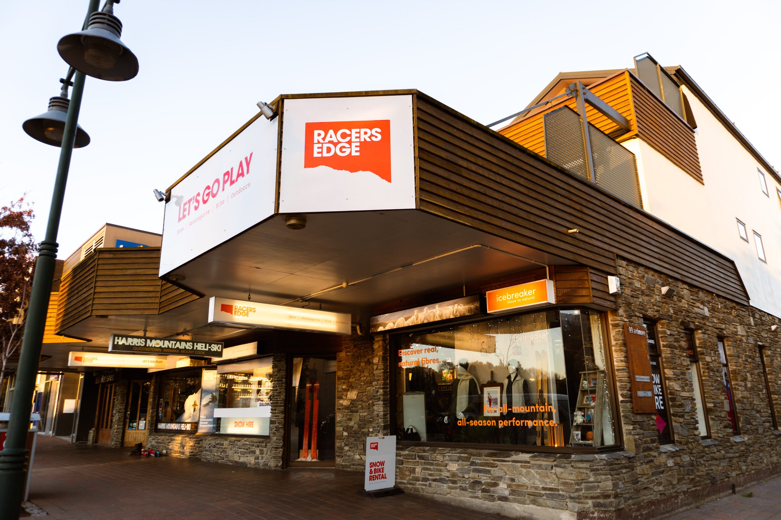 Racers Edge Wānaka storefront, a Love Wanaka Impact Partner, showcasing their outdoor retail location at dusk with illuminated signage on Mount Aspiring Road