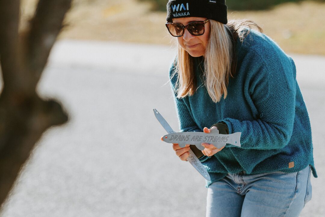 WAI Wānaka volunteer installing a 'Drains are Streams' marker to raise awareness about stormwater pollution in Wanaka, NZ