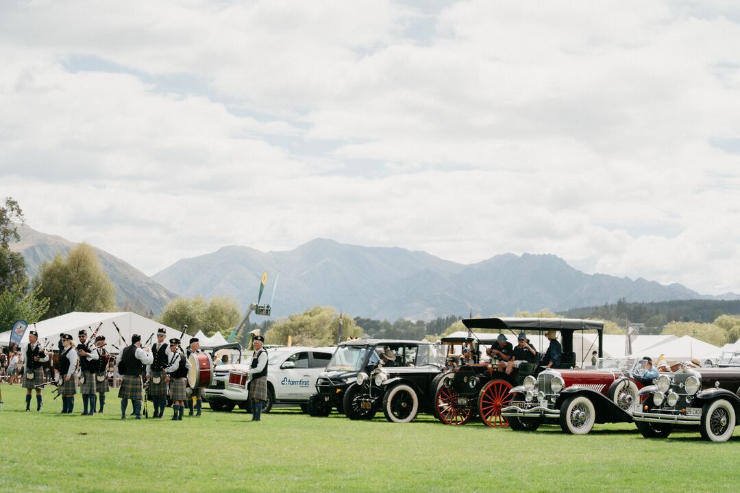 Cars on display at Wānaka A&P Show with bagpipe crew in foreground