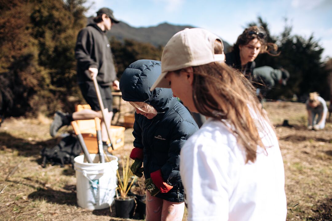 Young volunteers planting native species at Te Kākano Trust community day, with Mount Iron backdrop in Wānaka