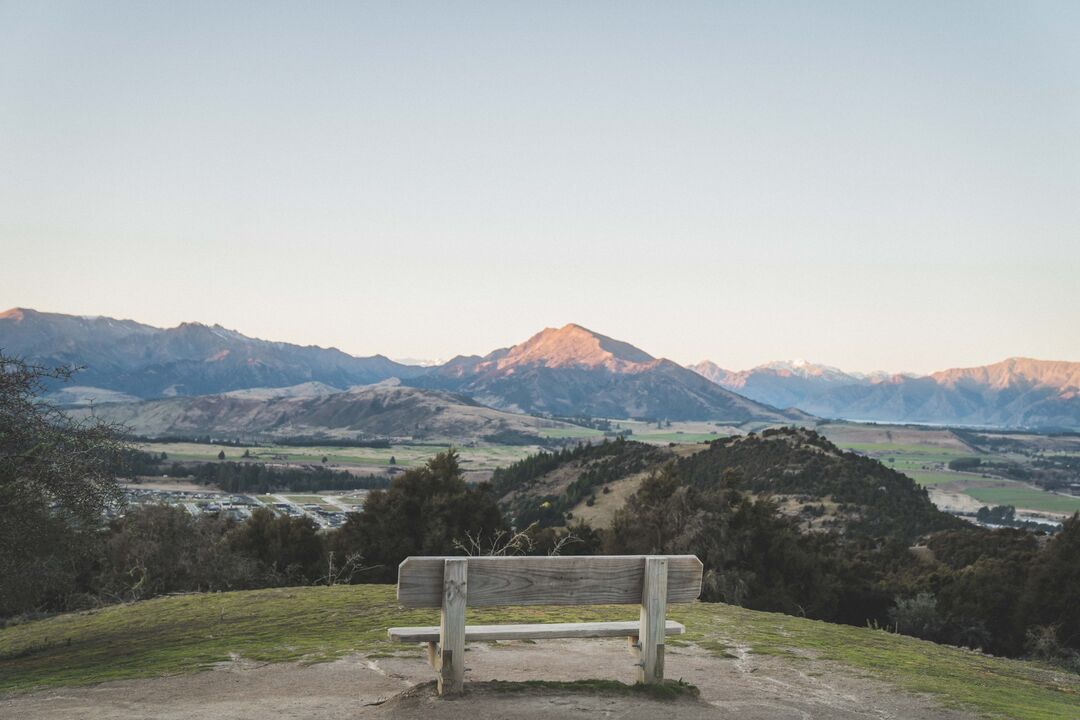 Wooden bench at Mount Iron summit overlooking Mount Maude and the Southern Alps, with Albert Town township nestled in valley below
