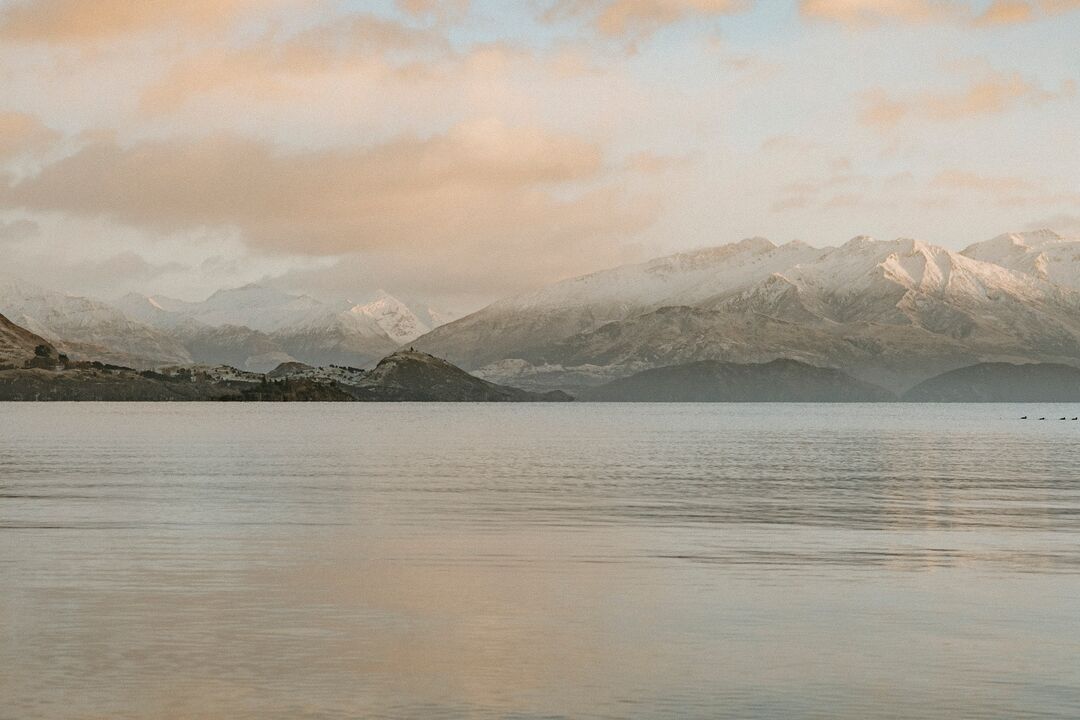 Lake Wanaka at dusk, surrounded snow capped mountains.
