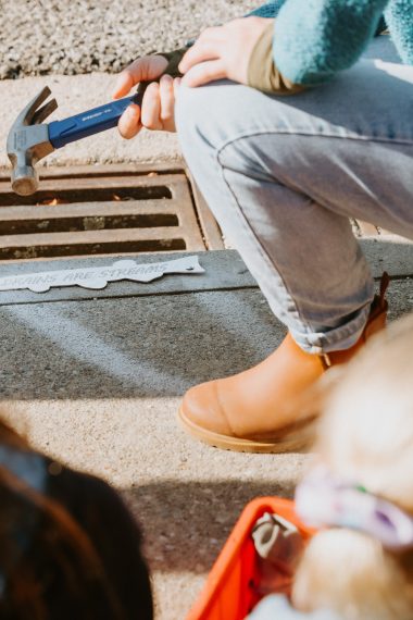 WAI Wānaka volunteer hammering a 'Drains are Streams' marker onto a stormwater drain in Wanaka NZ
