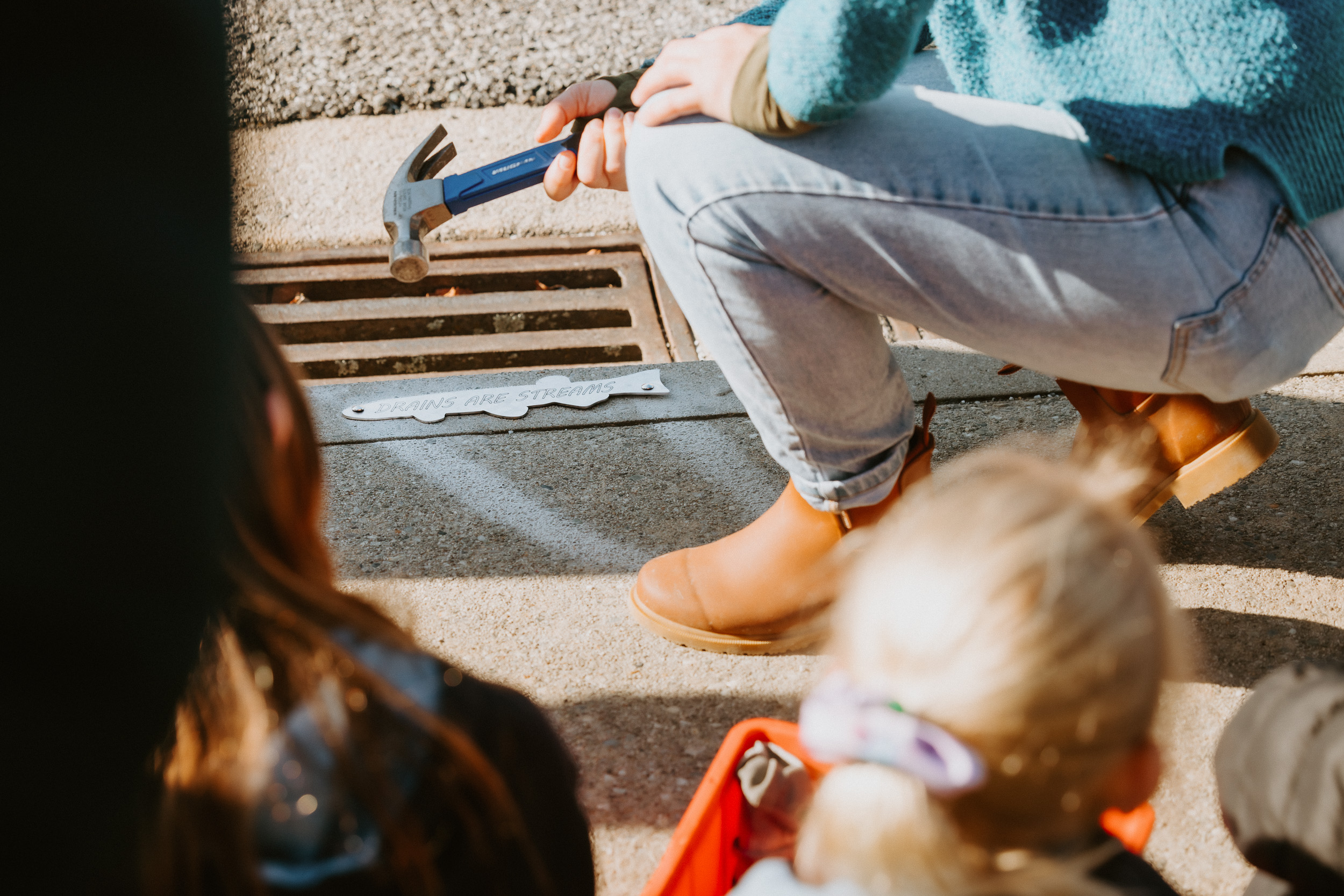 WAI Wānaka volunteer hammering a 'Drains are Streams' marker onto a stormwater drain in Wanaka NZ