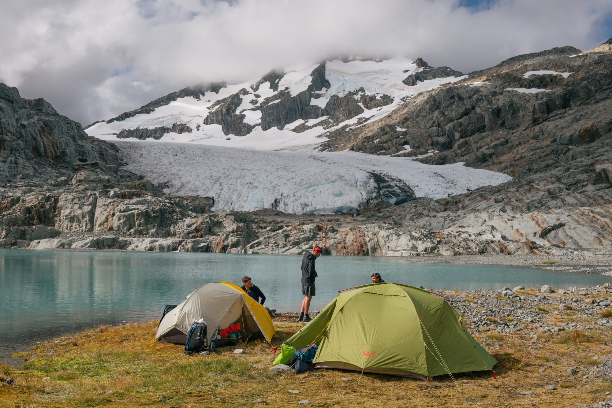 Camping tents by an alpine glacier lake with snow-capped mountains on the Brewster Track in Wānaka New Zealand