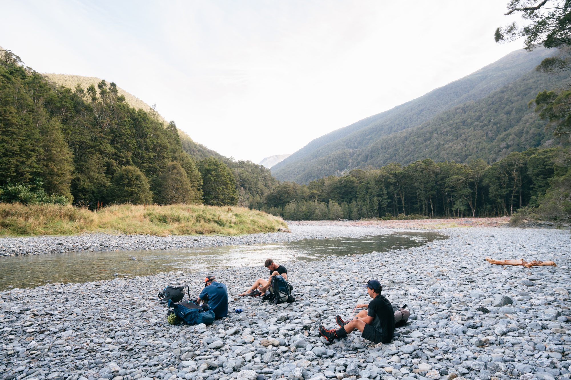 Group of trampers resting on rocky riverbed surrounded by native beech forest in Matukituki Valley, Wānaka