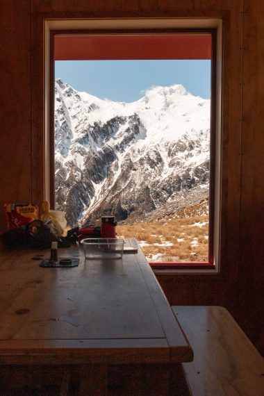 Mountain hut window view of snow-capped peaks in Mount Aspiring National Park, Wānaka backcountry winter adventure