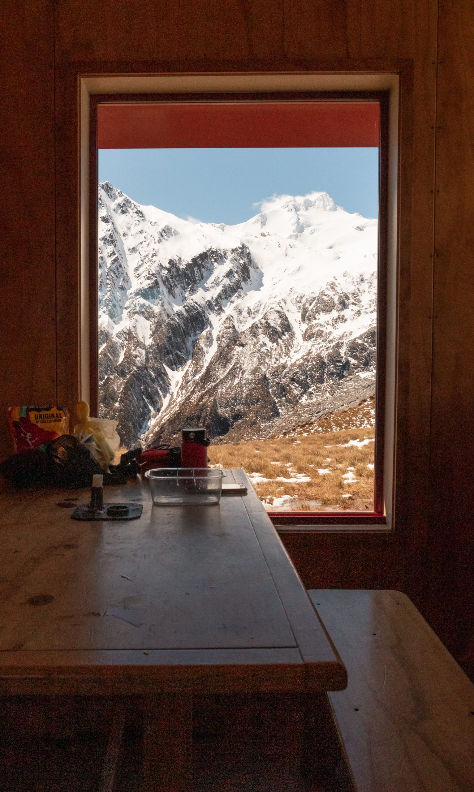 Mountain hut window view of snow-capped peaks in Mount Aspiring National Park, Wānaka backcountry winter adventure