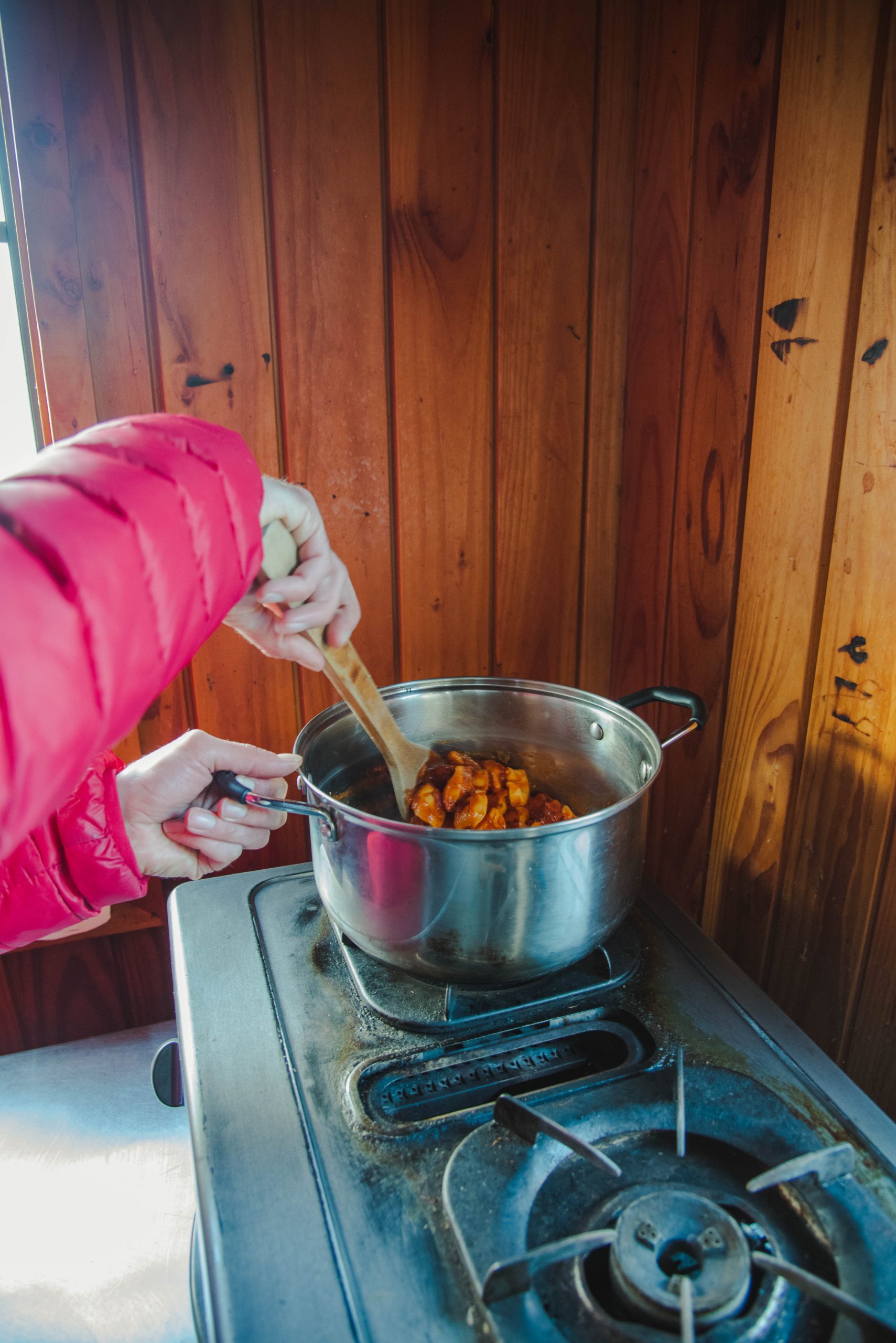 Person cooking in rustic alpine hut kitchen during winter hiking trip in Wānaka backcountry, New Zealand