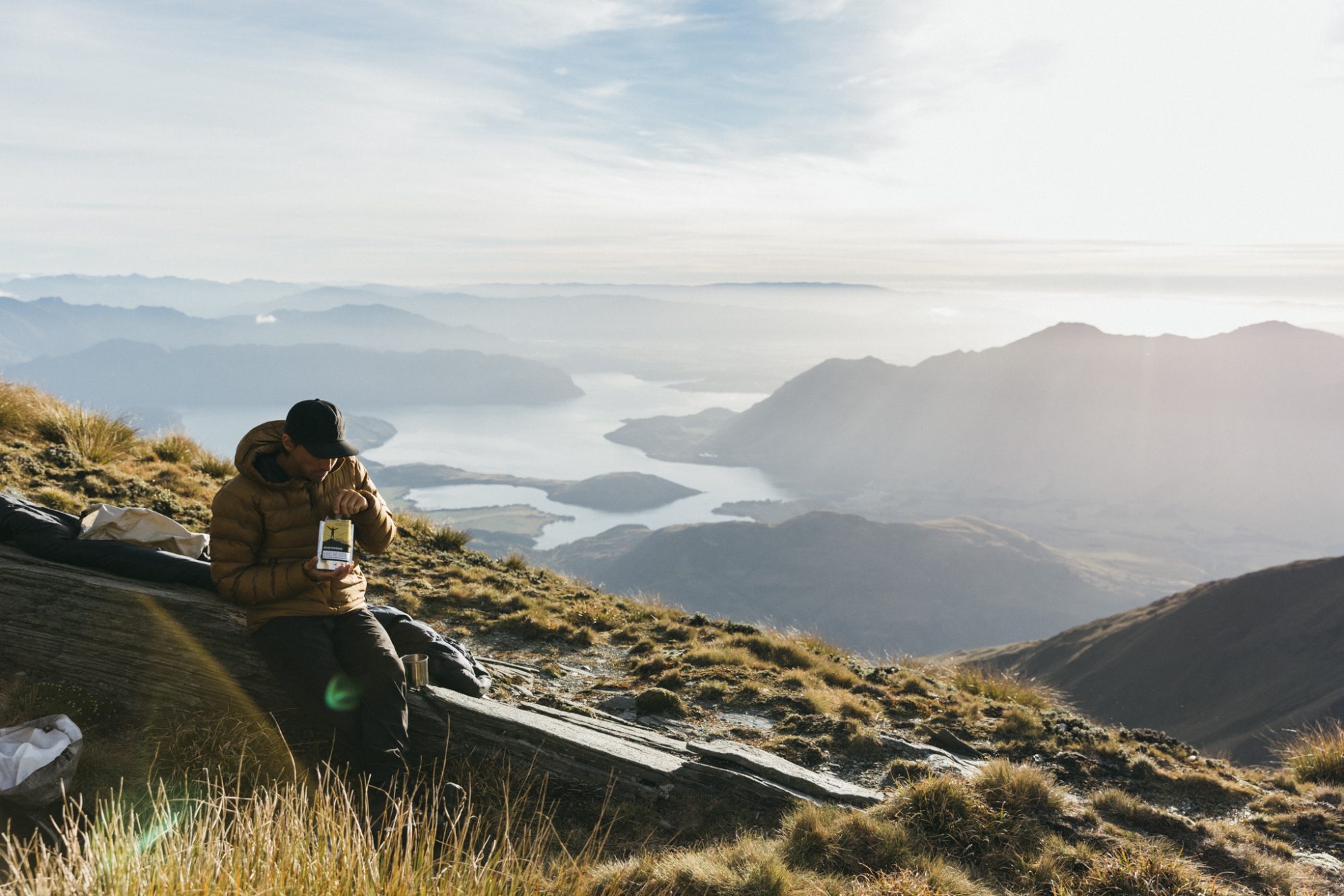 Hiker enjoying breakfast with breathtaking view of Lake Wānaka from mountain summit, South Island New Zealand
