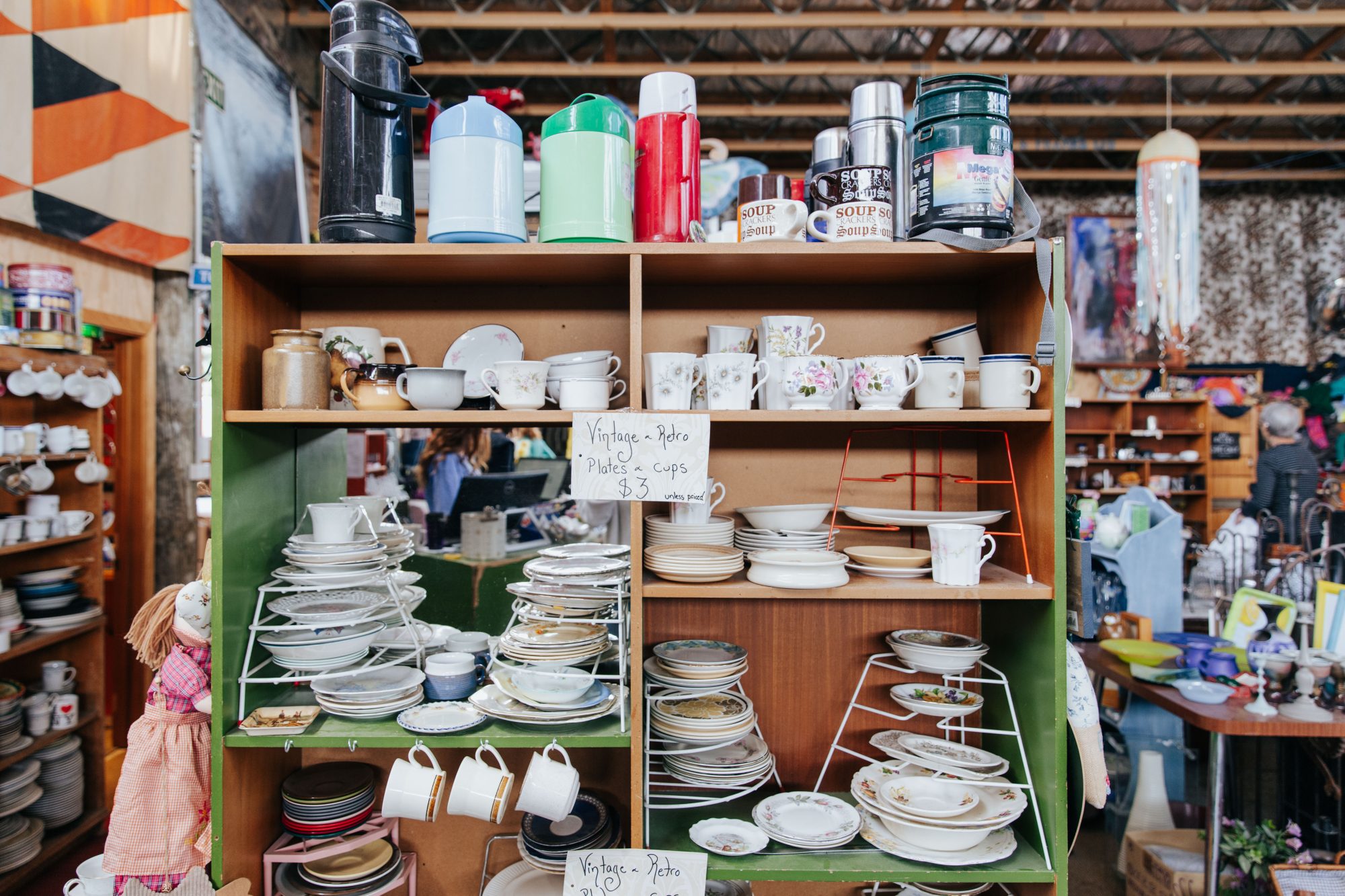 Neat display of crockery, jugs, and kitchenware stacked on wooden shelves inside Wastebusters.