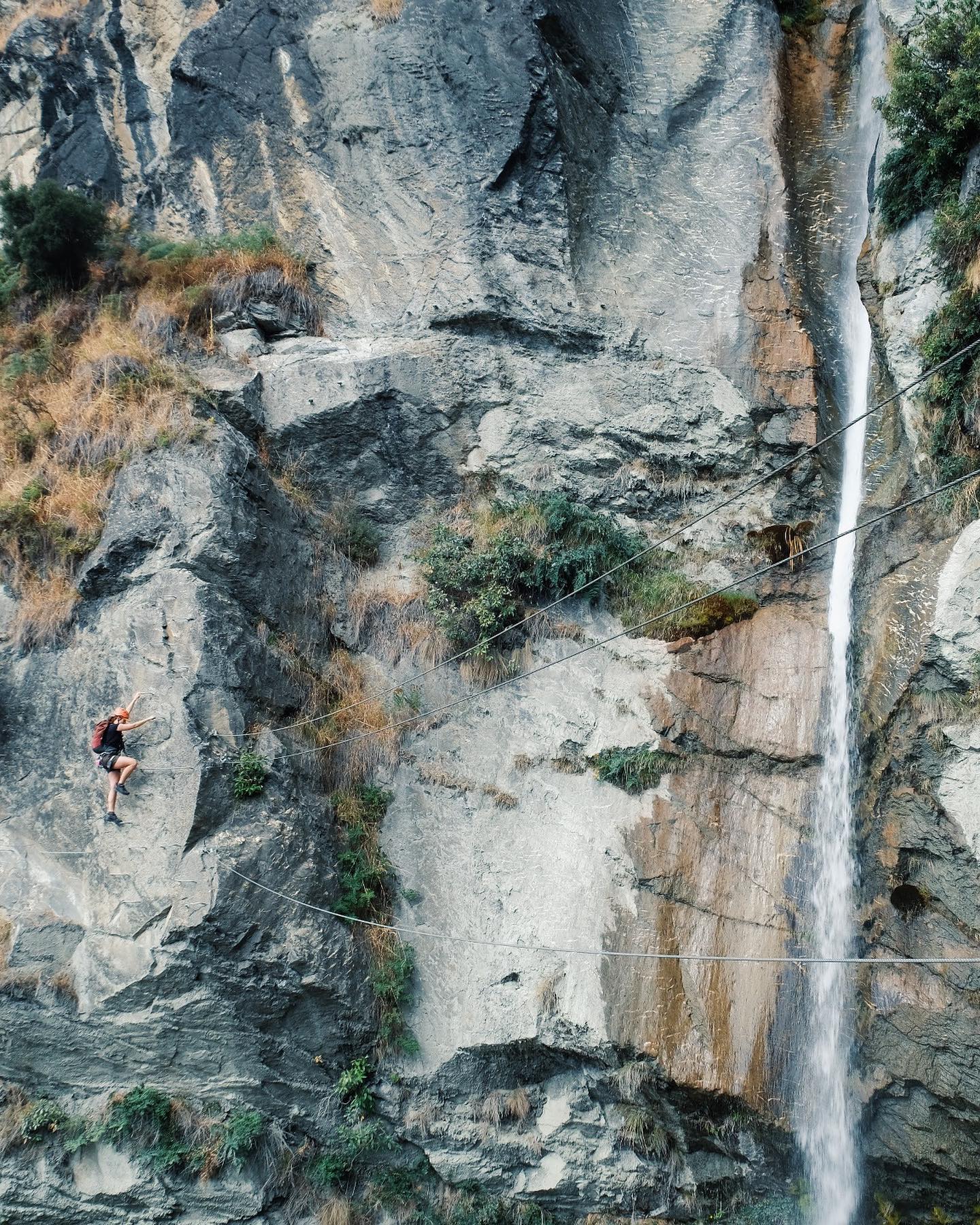 A climber on a rockface beside a water fall at Wildwire, in Wānaka, New Zealand