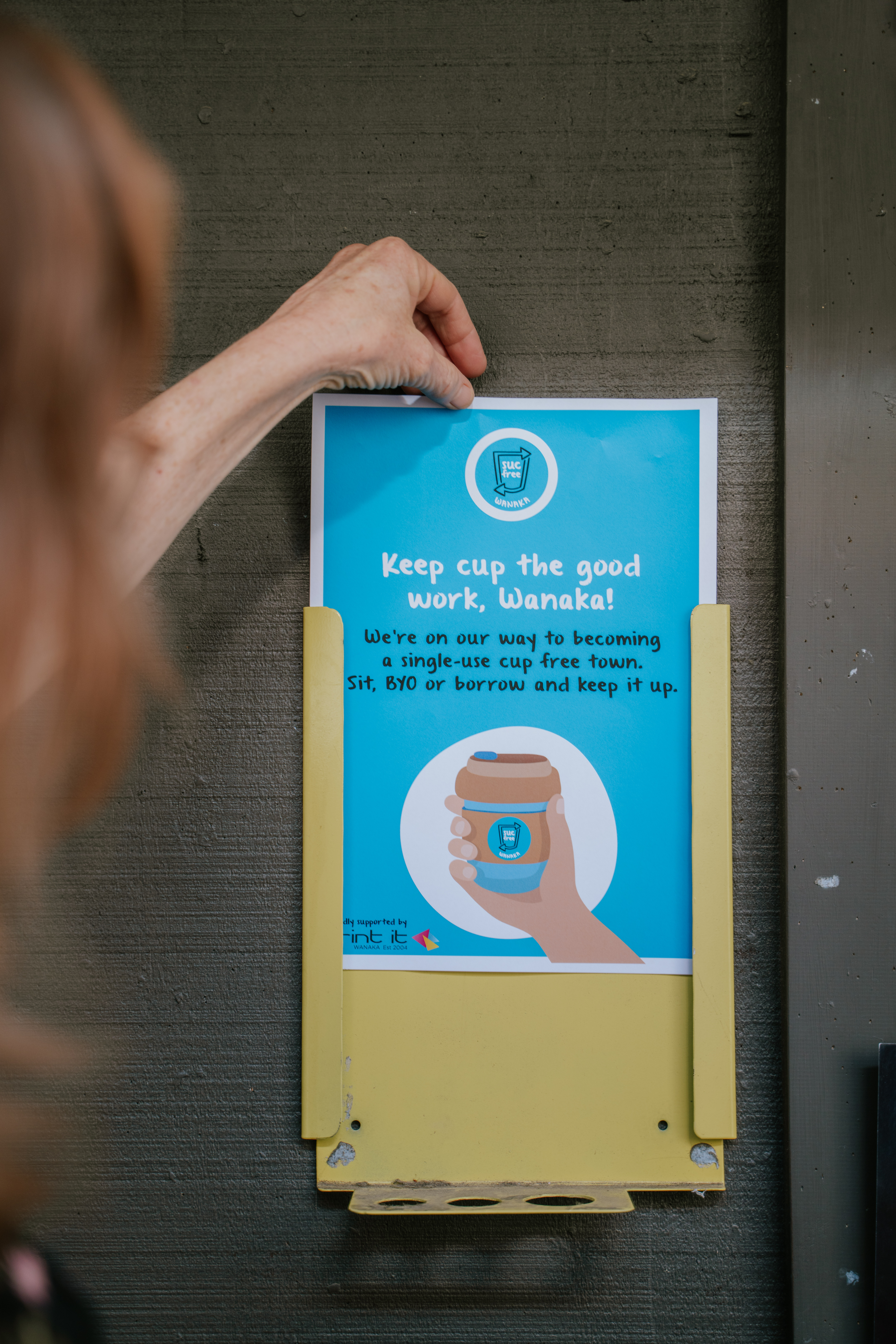 A hand putting a plastic free Wānaka polster into a yellow holder at Federal Diner in Wānaka New Zealand